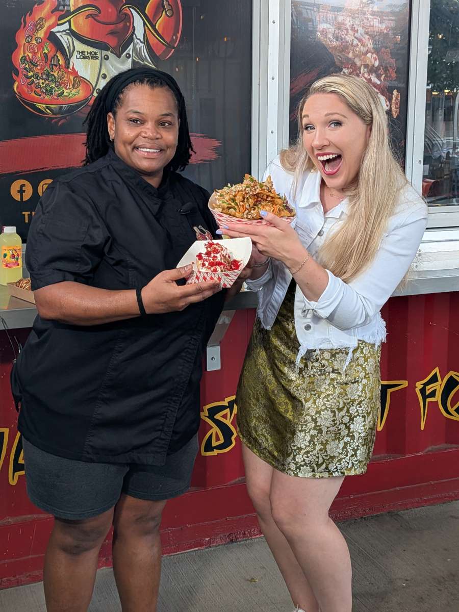 Chef Lakisha Powell and an Access Carolina reporter hold The Wok Lobster dishes in front of the Gather GVL kitchen